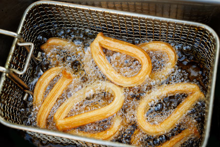 A close up of crispy churros frying in hot oil in a metal basketの写真素材