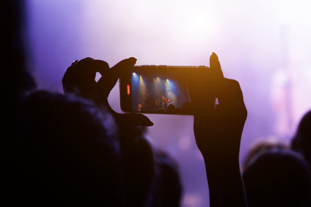 A crowd enjoying a popular music concert with stage lights and smartphones.の写真素材