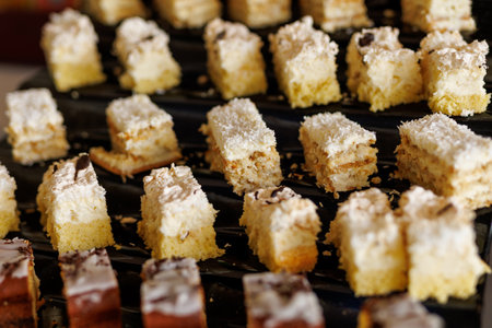 Bite-sized coconut cakes with white frosting on a black trayの写真素材