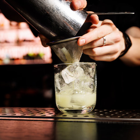 Bartender pours a mixed cocktail into a glass with ice.
