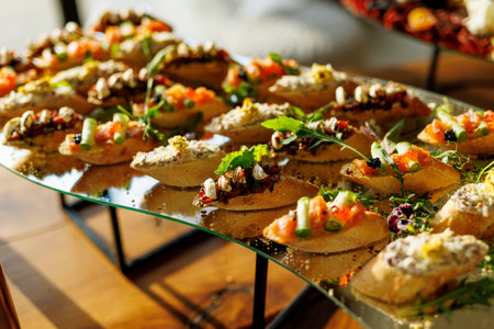 A vibrant array of gourmet bruschetta topped with fresh ingredients like salmon, cheese, and herbs, beautifully garnished with edible flowers on a glass serving trayの写真素材