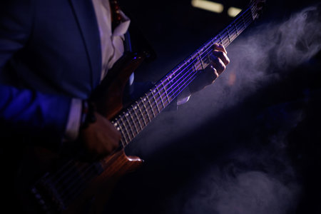 A musician strumming an electric bass guitar on a dimly lit concert stage.の写真素材