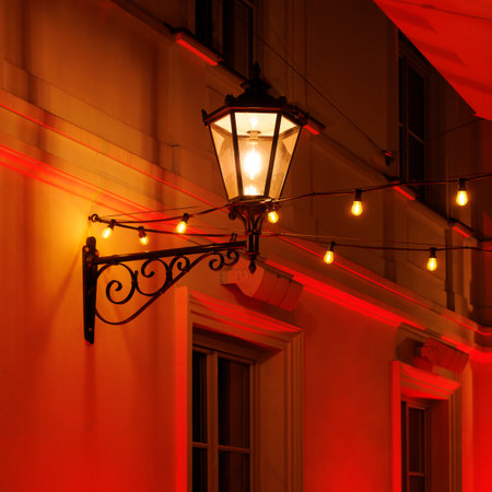 A vintage street lamp emits a warm glow, casting soft light on an old building facade.の写真素材