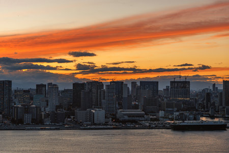 A vibrant sunset gloriously paints the evening sky above a lively and bustling city skyline situated by the waterの写真素材