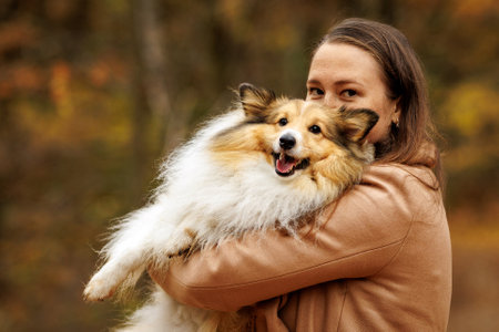 Girl holding a dog in her arms in an autumn forestの写真素材