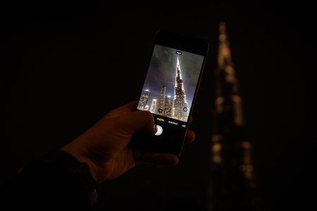 A hand holding a modern smartphone captures Dubai view of a glowing tower at nightの写真素材