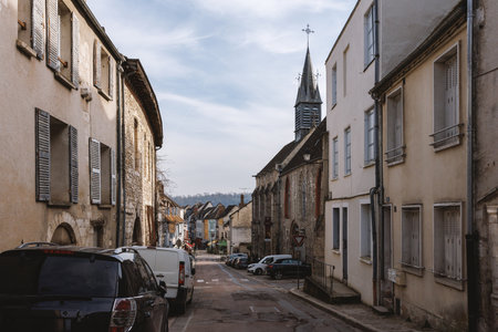 A narrow street with a church in the background. The street is lined with buildings and parked carsの写真素材