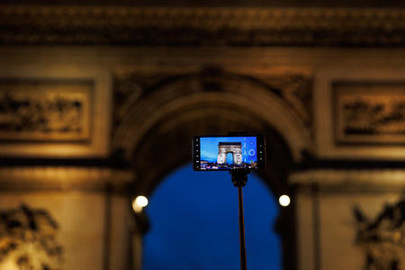 A tourist takes a photo of the Arc de Triomphe in Paris using a mobile phone on a monopodの写真素材