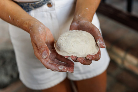 A woman is holding a dough ball in her hands. The dough ball is white and he is made of flour