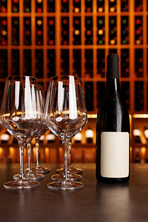 A bottle of wine is on a table next to four wine glasses. The scene is set in a bar or restaurantの写真素材