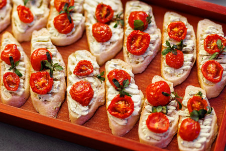 A tray of bread with tomatoes and herbs on top. The bread is sliced and arranged in a neat rowの写真素材