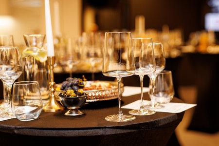 Close-up of empty wine glasses on a cocktail table with olives, grapes, and snacks. Elegant indoor event setup.の写真素材