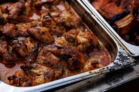Juicy grilled chicken wings covered in sauce, served in a metal tray. Outdoor food event.
