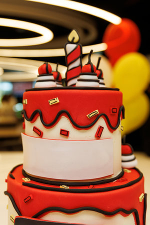 Colorful birthday cake with red and white fondant, large striped candle and confetti-like elements....
