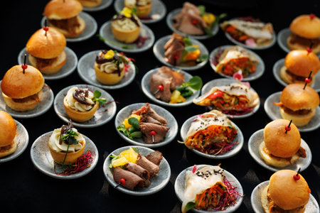 Various mini bites including sliders, beef slices, vegetable rolls, and canapes arranged on small plates. Ideal for catering, events, or receptions.の写真素材
