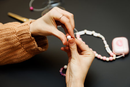Hands holding bead for making jewelry on black surface
