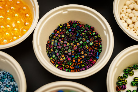 Colorful letter beads in bowl on black background for handmade craftsの写真素材