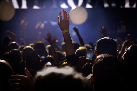 Close-up of a hand raised above a packed concert audience with warm stage lighting