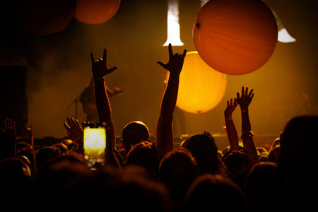 Silhouetted hand reaching up at a live music event, illuminated by dramatic stage lighting. Symbolizes unity, excitement, and immersive concert atmosphere.の写真素材