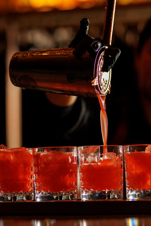 Close-up of a bartender pouring a red cocktail into several glasses filled with ice. Perfect for...