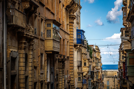 Traditional Maltese balconies in bright sunlight with a distant view of the sea in Valletta. Great for travel, architecture, and Mediterranean lifestyle imagery.の写真素材