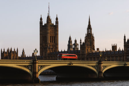 Iconic red bus crossing Westminster Bridge with the Palace of Westminster in background at golden...