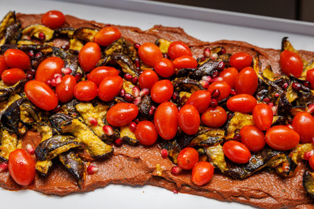 Catering platter with roasted eggplant strips, cherry tomatoes and pomegranate seeds spread over a red vegetable puree.の写真素材