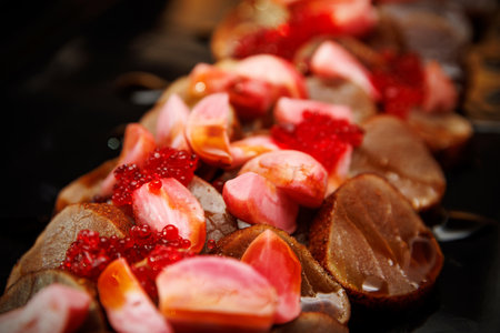 Tight macro of sliced cured meat topped with pink vegetable pieces and red pearls on dark plate.の写真素材
