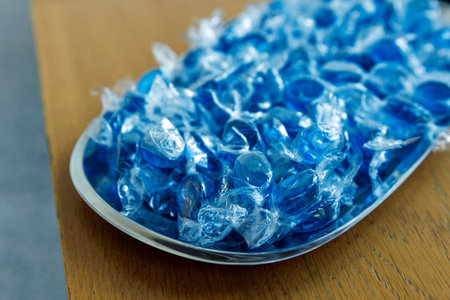 Pile of individually wrapped blue hard candies arranged on a metal tray on a wooden table.の写真素材