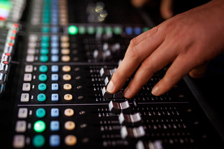 Audio engineer controlling sound levels on a professional mixing console with illuminated buttons and sliders.の写真素材