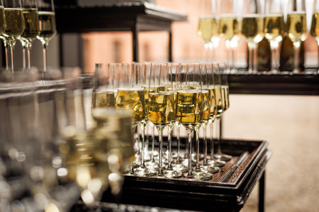 Hand pouring sparkling wine into a glass surrounded by empty flutes during a party preparation.