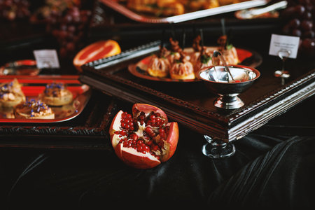 Pomegranate halves and various appetizers arranged on dark catering table with elegant trays.の写真素材