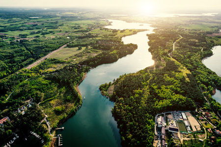 Aerial view of winding river and connected lakes surrounded by green forest and fields under evening sunlight.の写真素材
