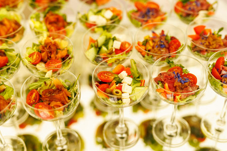 Colorful mixed vegetable salads with cherry tomatoes, cucumber, feta cheese, and greens served in cocktail glasses.の写真素材