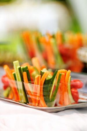Sliced carrots and cucumbers neatly arranged in transparent cups on a metal tray at a catering...