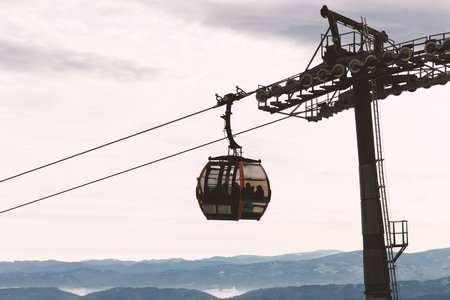 A gondola lift suspended above winter mountains. The cable car travels across a snowy alpine valley under cloudy sky.の写真素材
