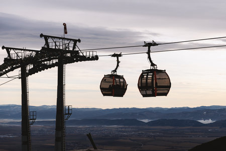 Silhouette of ski gondola cabins moving above mountain valley at winter ski resort.の写真素材