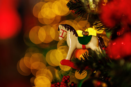 A small, detailed white and brown rocking horse figurine, painted with green and red accents, hangs from a green Christmas tree branch.の写真素材