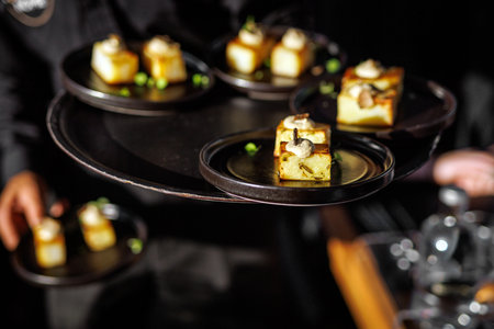 Small square appetizers served on trays by a waiter, captured during event catering.の写真素材