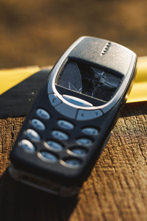 Old mobile phone with cracked screen on wooden surface