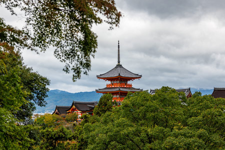 The iconic three-story pagoda stands out against a cloudy sky in Kyoto. Lush green and early autumn foliage frame the traditional architecture.の写真素材