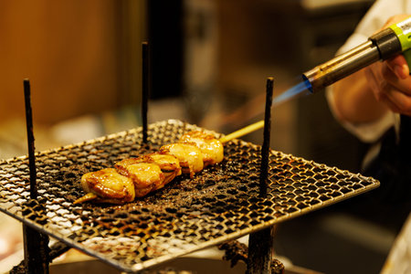A close-up of a blue flame from a culinary torch searing a skewer of fresh scallops on a metal rack.の写真素材