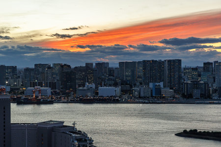 A wide cityscape view at dusk featuring high-rise buildings and a harbor under a vibrant orange sky.の写真素材