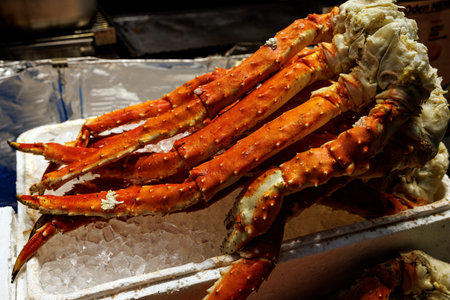 Fresh, bright orange king crab legs are piled on a bed of crushed ice in a white foam container.の写真素材