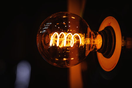 A detailed close-up of a glowing vintage-style filament bulb against a dark background.の写真素材