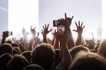 Large crowd of people with hands in the air and holding phones at a music festival under high key white lighting.の写真素材