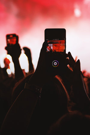 Vertical image of an audience member filming a live show on their phone, surrounded by a red glowing atmosphere.の写真素材