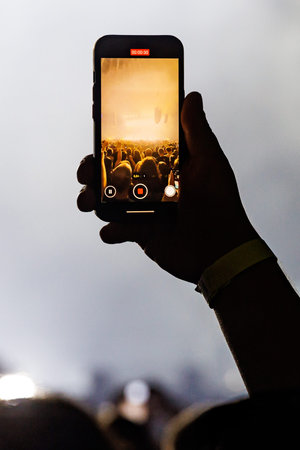 Close-up of a hand holding a mobile phone, capturing a live music festival stage with bright lights in vertical format.の写真素材