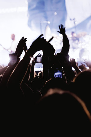 Crowds of people holding up mobile phones to film a live music performance. The silhouettes of hands...