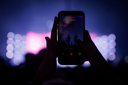 Vertical phone held by hands in a dark venue. The background features soft, out-of-focus purple and...
